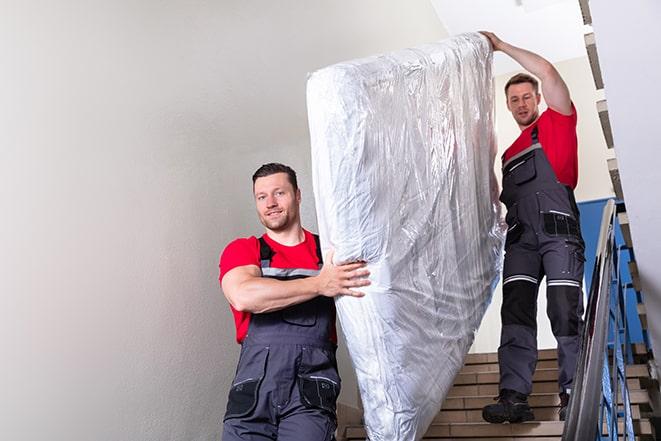 workers maneuvering a box spring through a narrow hallway in Jenks